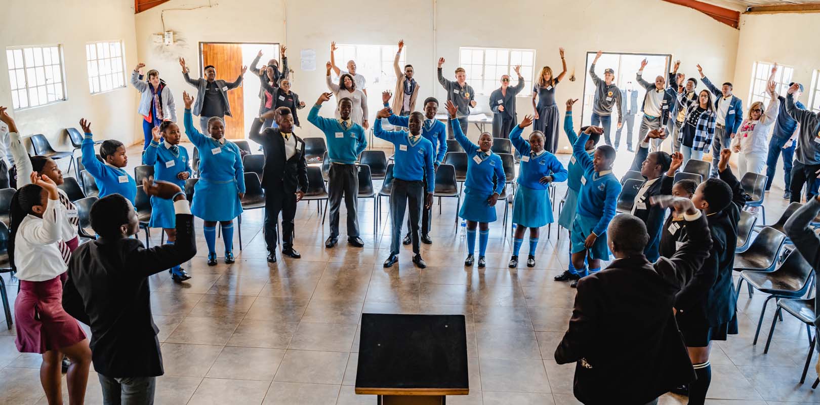 A group of students in a classroom standing and raising their hands